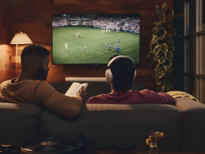Design-ohne-Titel-23 Twee mannen kijken voetbal, met de tv op de achtergrond in een donkere kamer en draagt de Sonos Ace hoofdtelefoon